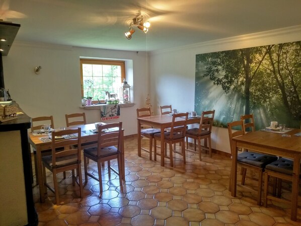 A dining area with hexagonal tiled flooring, wooden tables and chairs, a window with a view of greenery, and a wall mural of trees.