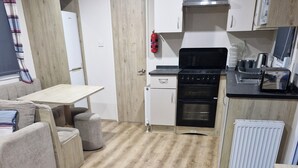 A modern kitchen with a wooden floor, a stove, a refrigerator, and a dining area with a table and chairs. - Highfield Grange Holiday Park
3 Bed Sleeps 8
 (Clacton-on-Sea)