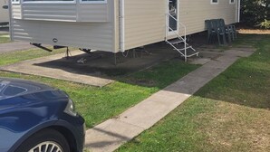 A mobile home with a covered porch, a satellite dish, and a small outdoor seating area. - Highfield Grange Holiday Park
3 Bed Sleeps 8
 (Clacton-on-Sea)