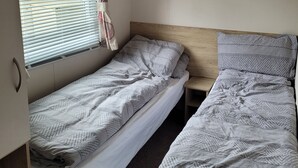 A small, compact room with two single beds, a window with blinds, and a curtain. - Highfield Grange Holiday Park
3 Bed Sleeps 8
 (Clacton-on-Sea)