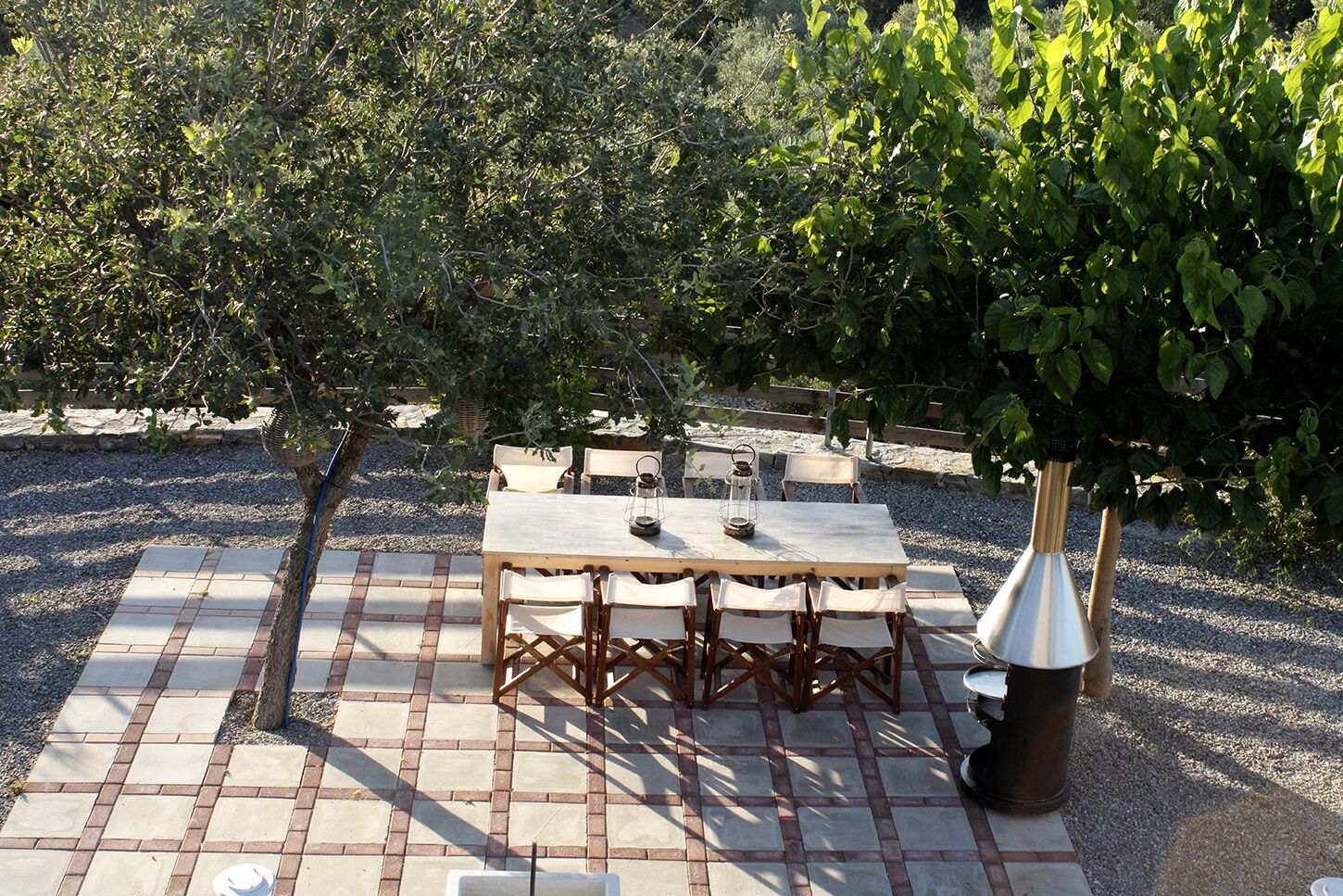 An outdoor patio with a wooden table and chairs, surrounded by gravel and plants.