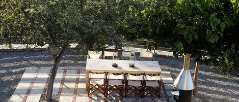 An outdoor patio with a wooden table and chairs, surrounded by gravel and plants.