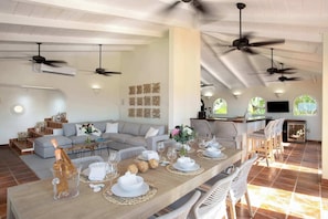 A spacious living area with a dining table set for a meal, a sofa, and a kitchen area with a TV. - Joie de Vivre (4 bedrooms) - Beachfront Baie Rouge villa with pool, Terres Basses, St. Martin (Les Terres Basses)