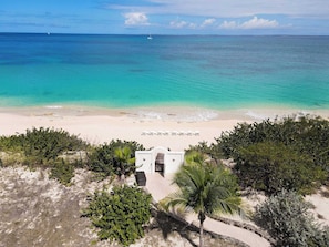 A beach view with a white building, palm trees, and a clear blue sea. - Joie de Vivre (4 bedrooms) - Beachfront Baie Rouge villa with pool, Terres Basses, St. Martin (Les Terres Basses)