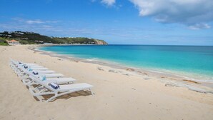 A beach with white lounge chairs lined up along the shore, a clear blue sky, and a calm sea. - Joie de Vivre (4 bedrooms) - Beachfront Baie Rouge villa with pool, Terres Basses, St. Martin (Les Terres Basses)