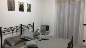 A bedroom with a bed, pillows, a bedside table with a lamp, a TV, and three paintings on the wall.