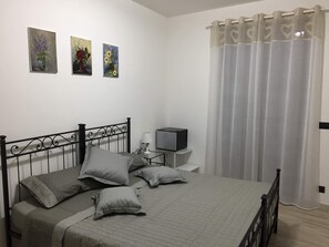 Un dormitorio con cama, almohadas, una mesita de noche con lámpara, un televisor y tres cuadros en la pared.