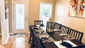 A dining area with a long table, chairs, and a chandelier. There are doors and windows with blinds. - FAMILY RETREAT/ PET FRIENDLY NEAR MILITARY BEACHES AND BASES (Jacksonville)