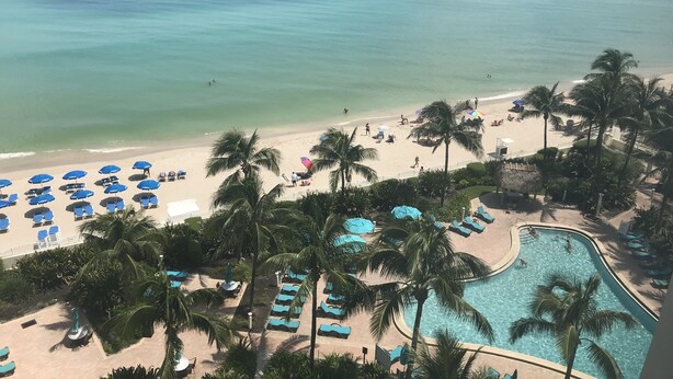 Un resort en la playa con piscina, palmeras y sombrillas.