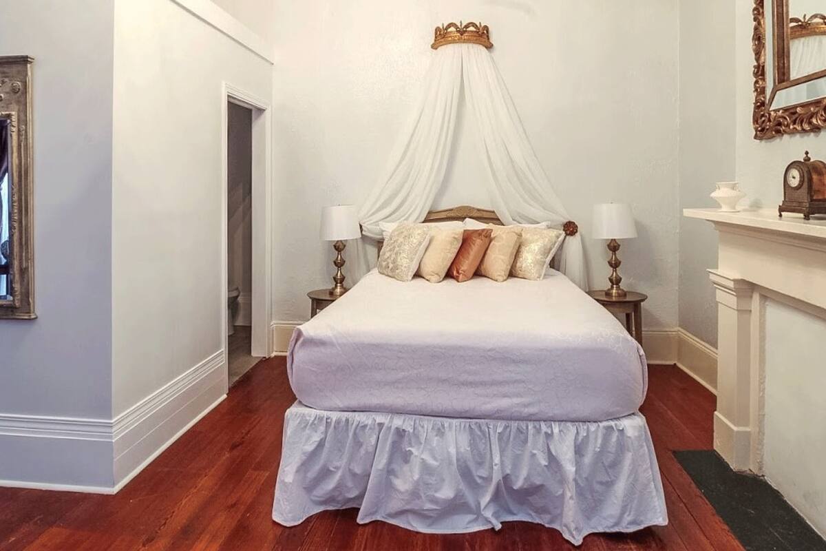 Une chambre à coucher avec un lit à baldaquin, des rideaux blancs et un miroir doté d’un cadre orné.
