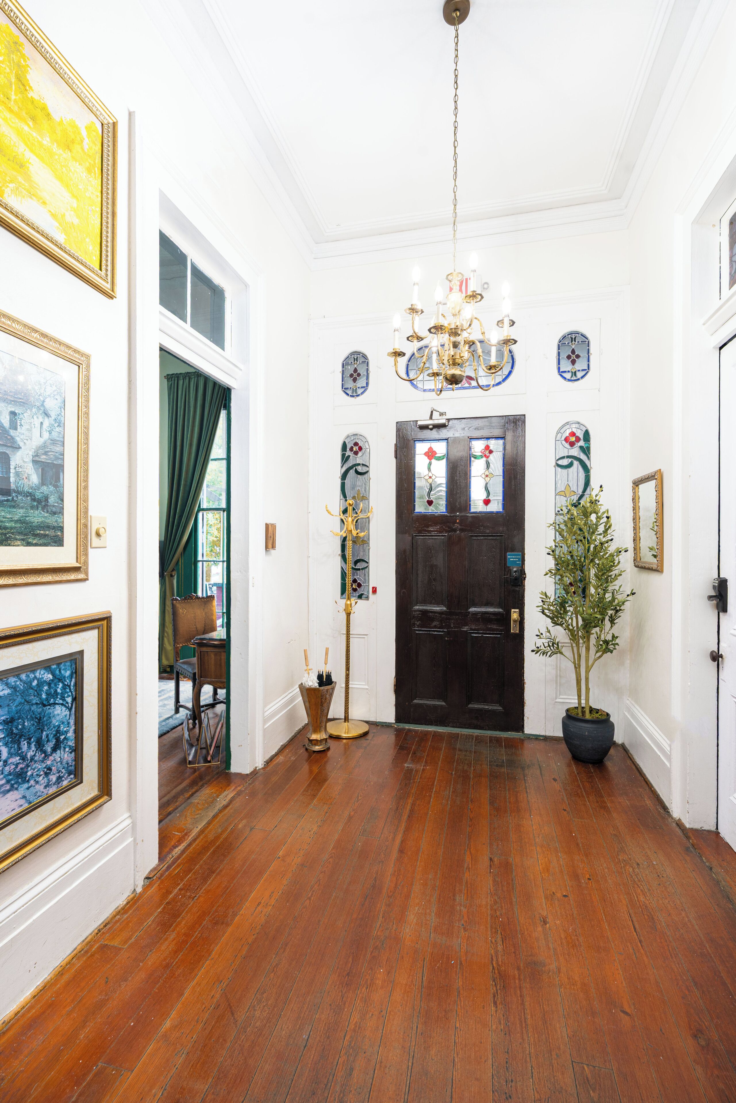 A hallway with wooden flooring, a chandelier, and a door with stained glass windows.