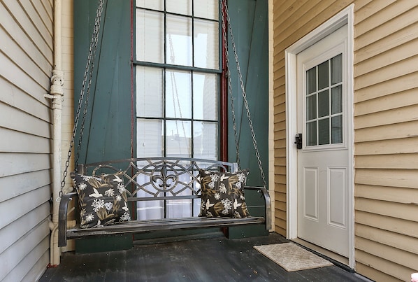 A porch with a swing seat and a door. - The Mansion on Royal (New Orleans)