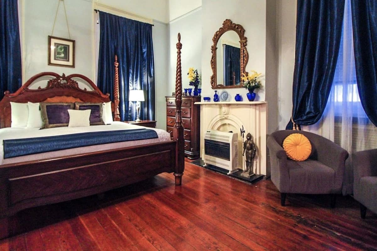 Une chambre à coucher avec un grand lit en bois, une cheminée, un miroir et deux fauteuils.