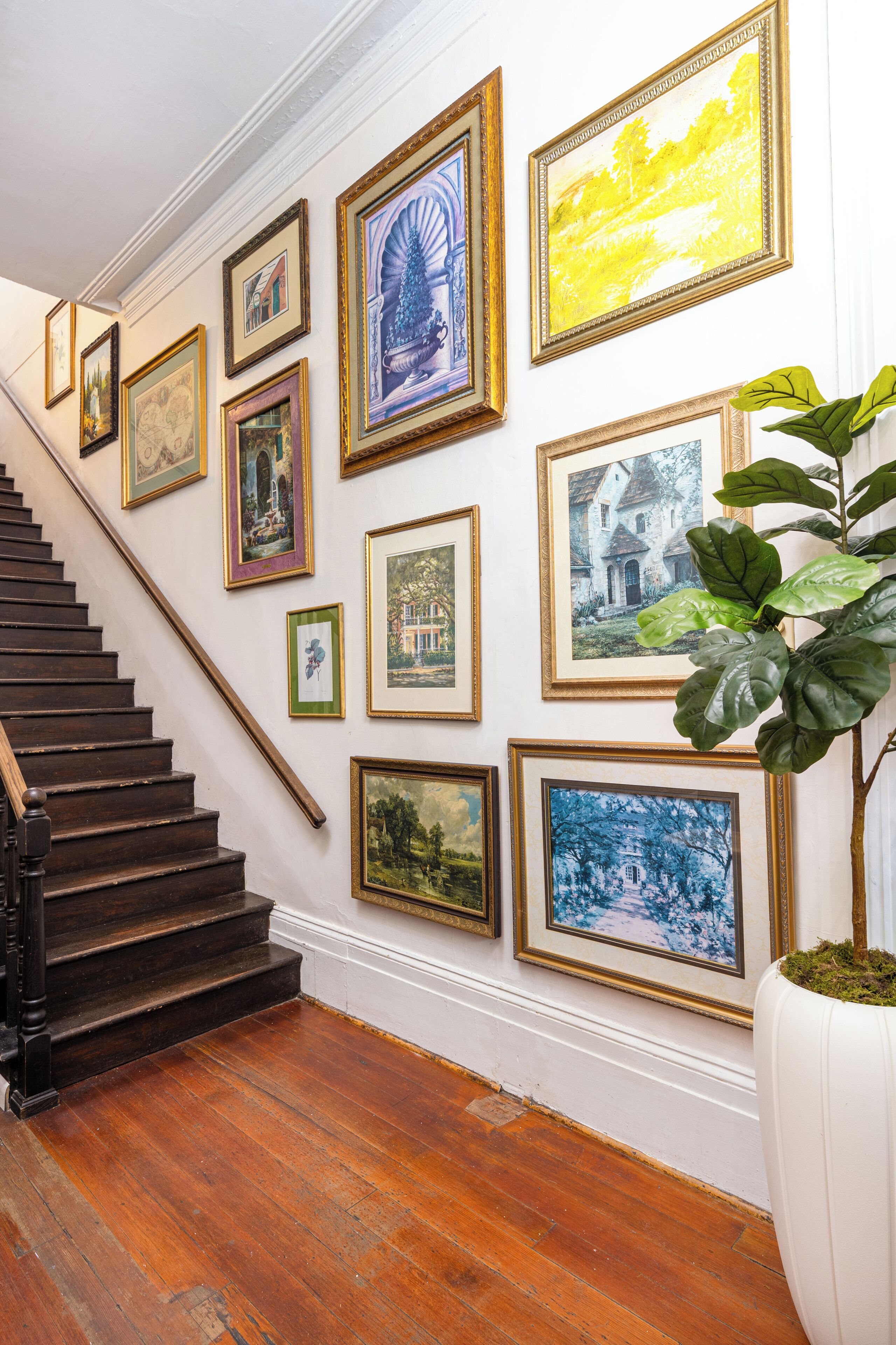 A staircase with a handrail leading to a landing where a collection of framed artworks is displayed on the wall.