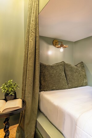 A room with a bed, a bedside table with a book and a plant, and a curtain. - The Mansion on Royal (New Orleans)