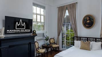 A hotel room with a bed, a television, a chandelier, a painting, and a view of the outdoors.