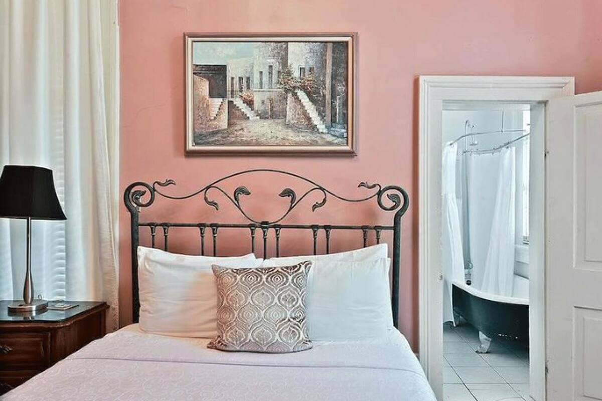 Une chambre à coucher avec un lit, une table de chevet, une lampe, un tableau encadré au mur et une porte de salle de bain.