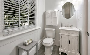 A bathroom with a toilet, sink, and window with blinds. - The Mansion on Royal (New Orleans)