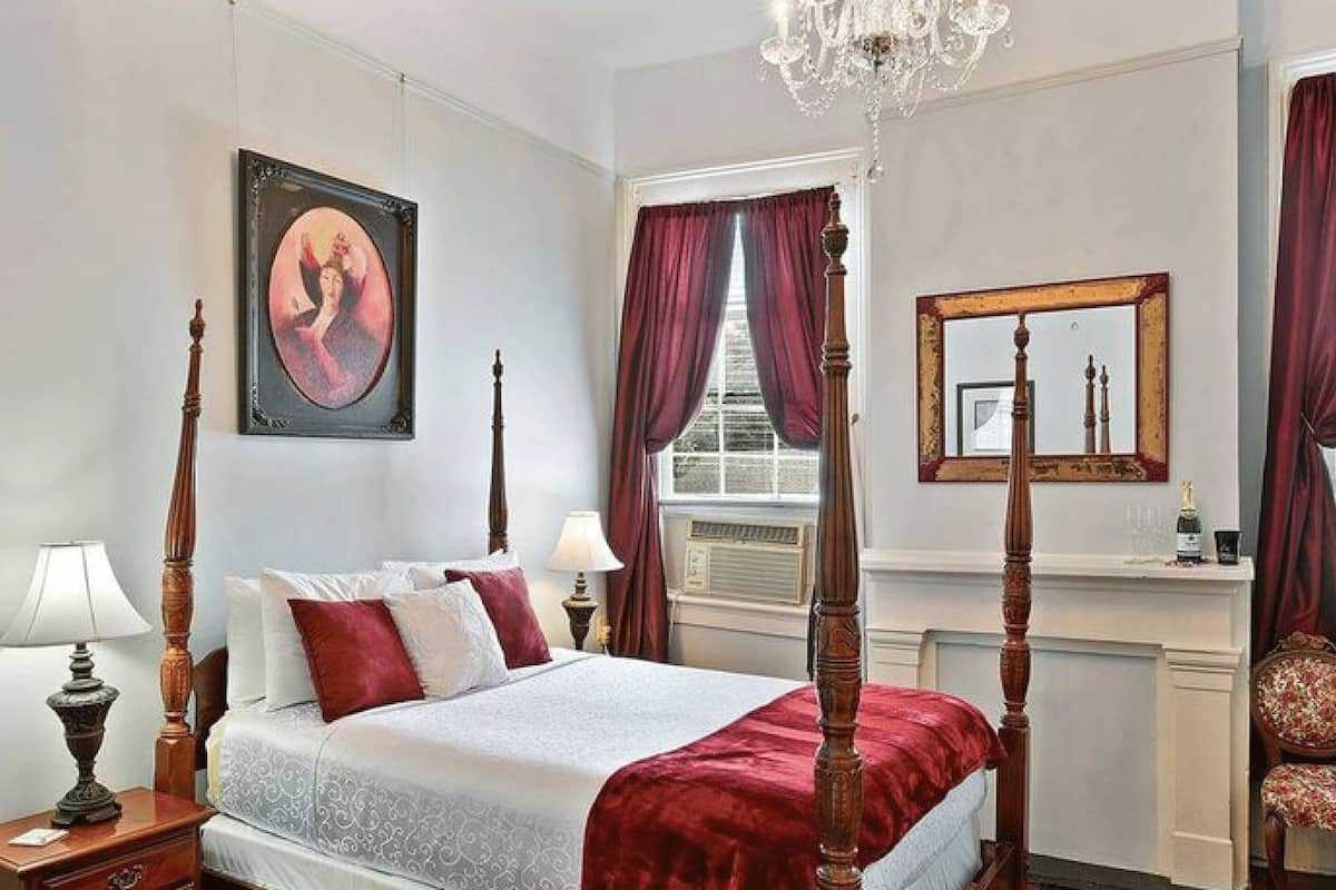 Un lit à baldaquin avec une couvre-lit rouge, un lustre, un tableau encadré et un miroir au mur.