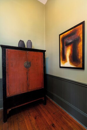 A room with a wooden cabinet, a framed abstract painting, and a radiator. - The Mansion on Royal (New Orleans)