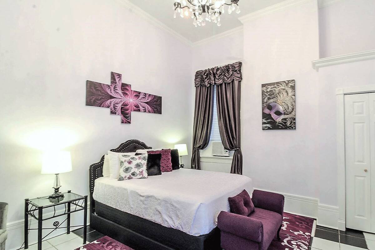 Une chambre à coucher avec un lit, une chaise, une lampe et des œuvres d’art accrochées aux murs.