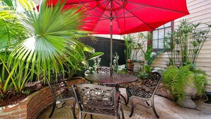 A patio with a round table and four chairs, a red umbrella, and various potted plants. - The Mansion on Royal (New Orleans)