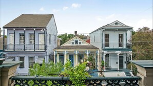 A row of three-story buildings with balconies, a central building with a porch, and a green railing in the foreground. - The Mansion on Royal (New Orleans)