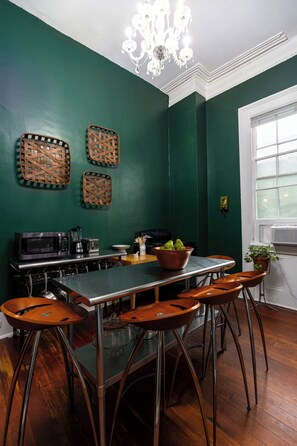 A kitchen with a central island, bar stools, a chandelier, and a window with blinds. - The Mansion on Royal (New Orleans)