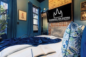 A hotel room with a bed, a window with curtains, a brick wall, and a framed picture on the wall.