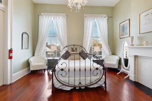 A bedroom with a metal bed frame, two white chairs, a fireplace, and a chandelier. - The Mansion on Royal (New Orleans)