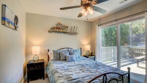 A bedroom with a bed, two bedside tables, a ceiling fan, a large window, and a balcony. - Cozy Cottage 3 beds 2 baths W/ Outdoor grill! (North Beach)