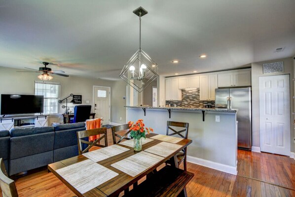 A modern kitchen with a central island, a dining area with a wooden table, and a living room with a sofa and a TV.