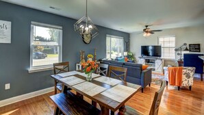 A dining area with a table, chairs, and a chandelier. There is a living room with a sofa and a television. - Cozy Cottage 3 beds 2 baths W/ Outdoor grill! (North Beach)