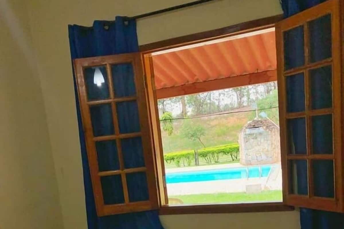Una habitación con cama, ventana con cortinas y vista a una piscina y follaje exterior.