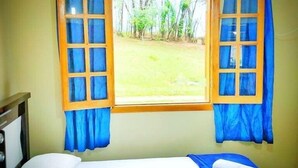 Una habitación con una cama, una ventana con cortinas azules y vistas a una zona con césped.