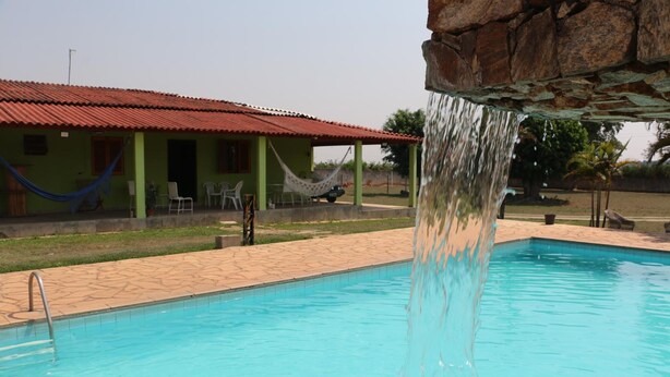 Una piscina con una cascada, una hamaca y un edificio de techo rojo al fondo.