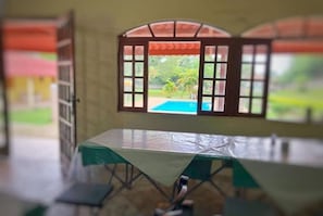 A room with a view of a swimming pool through a window with a wooden frame.