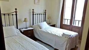 A bedroom with two single beds, wooden nightstands, and a window with curtains.