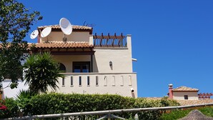 A two-story building with a satellite dish, a balcony, and a small attached structure with a chimney.