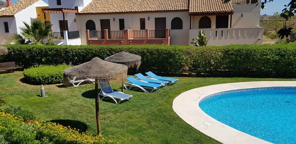 A pool area with lounge chairs, a small pool, and a building with a tiled roof in the background.