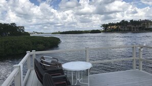 Eine Terrasse mit Stühlen und Tisch, die auf ein Gewässer mit Blick auf die Küstenlinie und Gebäude in der Ferne blickt.