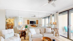 A spacious living room with a sofa, armchairs, a coffee table, and a TV. There is a dining area with chairs and a table in the background. - Summer House on Romar Beach (Orange Beach)
