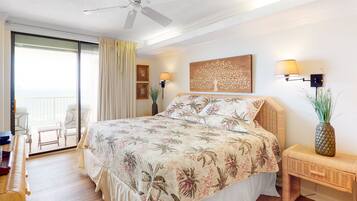 A bedroom with a bed, a ceiling fan, a nightstand with a lamp, a wall art piece, and a view of the balcony.