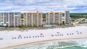 A beachfront hotel with multiple high-rise buildings, a sandy beach with blue lounge chairs, and a pool area. - Summer House on Romar Beach (Orange Beach)
