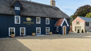 Um edifício tradicional com fachada escura e telhado de palha, exibindo uma placa com a inscrição 'Guinness Arms'.