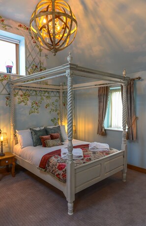 A four-poster bed with a floral bedspread, a hanging light fixture, and a window with curtains. - Guinness Arms (Bury St Edmunds)