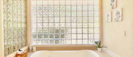 A bathroom with a large window, a bathtub, and a wicker basket.