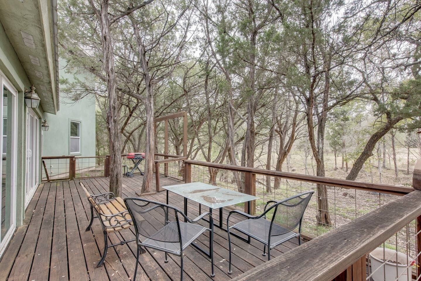 A wooden deck with outdoor furniture, including a table and chairs, overlooking a forested area.