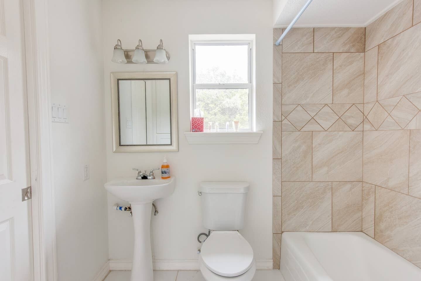 A bathroom with a pedestal sink, a toilet, a shower, and a window.