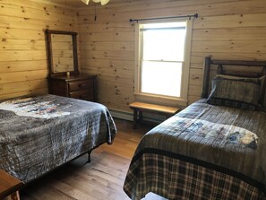 Ein Zimmer mit zwei Betten, Holzwänden, einem Fenster, einem Spiegel und einer hölzernen Bank.